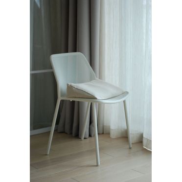 Poduszka klinowa w naturalnym odcieniu na białym krześle w jasnym, minimalistycznym wnętrzu.