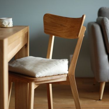 Poduszka klinowa na krześle w jasnym wnętrzu z drewnianym stołem i szarą sofą w tle.