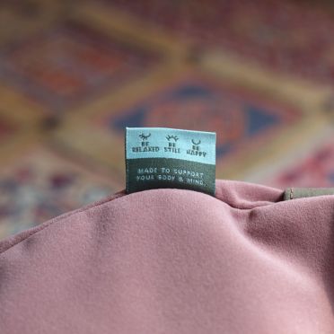 Zbliżenie na metkę poduszki w kolorze różowym z napisem „Made to support your body & mind” na tle kolorowego, orientalnego dywanu.