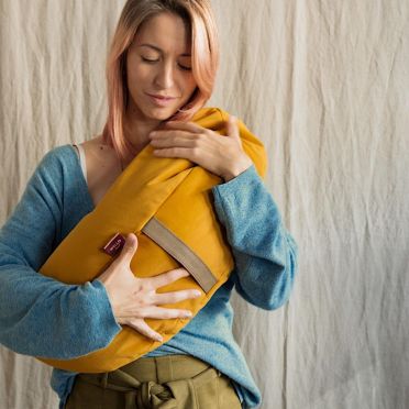 Kobieta tuli poduszkę w kształcie księżyca w ciepłym, musztardowym odcieniu żółci — idealną do bliskości i relaksu.