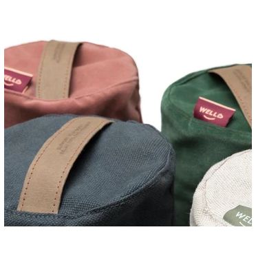 Cztery małe wałki gryczane w kolorach: grafitowym, różowym, zielonym i jasnym, ułożone w grupie. Widoczne uchwyty ze skóry wegańskiej z celulozy i metki marki WellB.