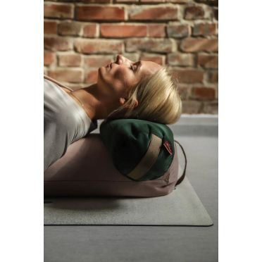 Kobieta opiera głowę na małym wałku gryczanym w zielonym kolorze, ułożonym na większym jasnoróżowym wałku – idealne podparcie do relaksu lub jogi.