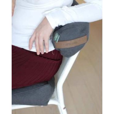 Kobieta siedząca na białym krześle z siedziskiem i małym wałkiem gryczanym w grafitowym pokrowcu pod pachą; widoczna metka i uchwyt ze skóry wegańskiej z celulozy.