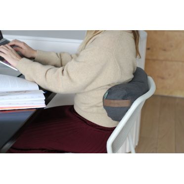 Kobieta pracuje przy komputerze, siedząc na krześle z małym wałkiem gryczanym WellB w kolorze terakoty za plecami jako podparcie.