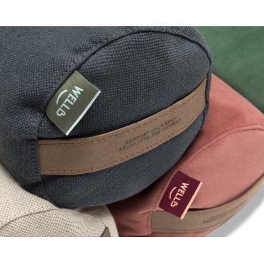 Trzy wałki bolstery do jogi WELLB w kolorach  plażowy biały,  grafitowym i pudrowym różu ułożone pionowo na białym tle, z widoczną skórzaną rączką i zieloną metką marki.