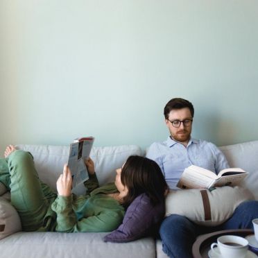 para ludzi siedząca na jasnej kanapie w przytulnym pokoju, na kolanach trzymają poduszki do relaksacji w kształcie księżyca