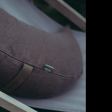 Zbliżenie na brązową lnianą poduszkę półksiężycową WellB umieszczoną na jasnym drewnianym leżaku, idealną do relaksu i medytacji.