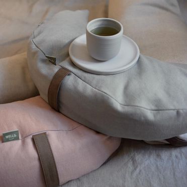 Dwie poduszki do medytacji i relaksacji w kształcie księżyca z lnu, na jednej z poduszek stoi filiżanka z kawą.