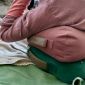 Osoba w różowej bluzie siedzi na różowej i zielonej poduszce do medytacji; tło stanowią zielony koc i beżowy pled.